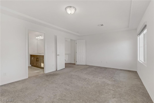 unfurnished bedroom with light carpet, ensuite bath, and a raised ceiling