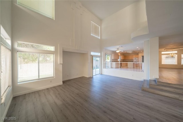 unfurnished living room with hardwood / wood-style flooring, ceiling fan, and a high ceiling