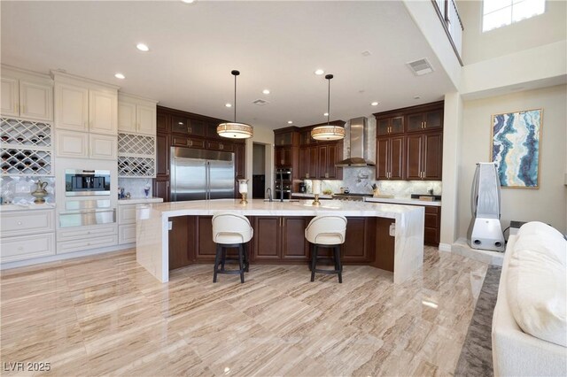 kitchen featuring wall chimney exhaust hood, stainless steel built in refrigerator, a breakfast bar, tasteful backsplash, and decorative light fixtures