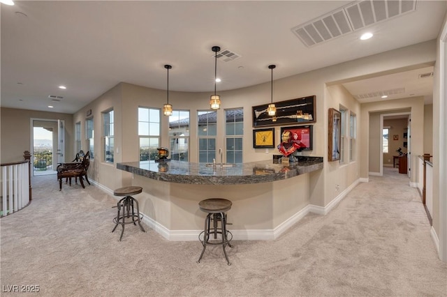 kitchen with sink, a breakfast bar area, decorative light fixtures, light carpet, and kitchen peninsula