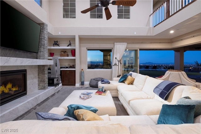 living room with a premium fireplace, a towering ceiling, built in features, and ceiling fan