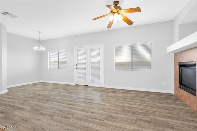 unfurnished living room with ceiling fan with notable chandelier, a fireplace, and light hardwood / wood-style floors