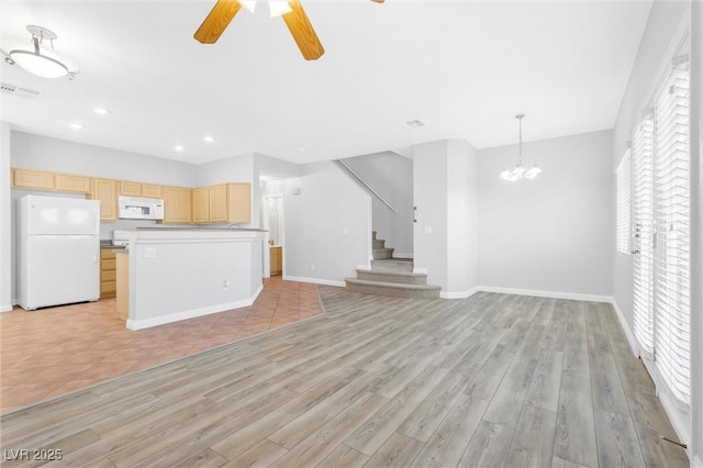 unfurnished living room with ceiling fan with notable chandelier and light hardwood / wood-style floors