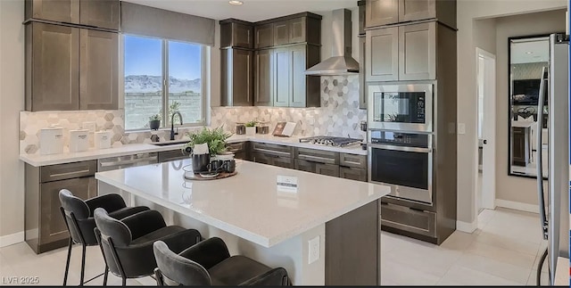 kitchen with stainless steel appliances, a center island, tasteful backsplash, a kitchen bar, and wall chimney exhaust hood