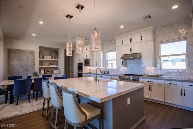 kitchen with pendant lighting, white cabinetry, a kitchen island with sink, stainless steel appliances, and light stone countertops