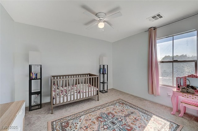 carpeted bedroom featuring ceiling fan and a crib