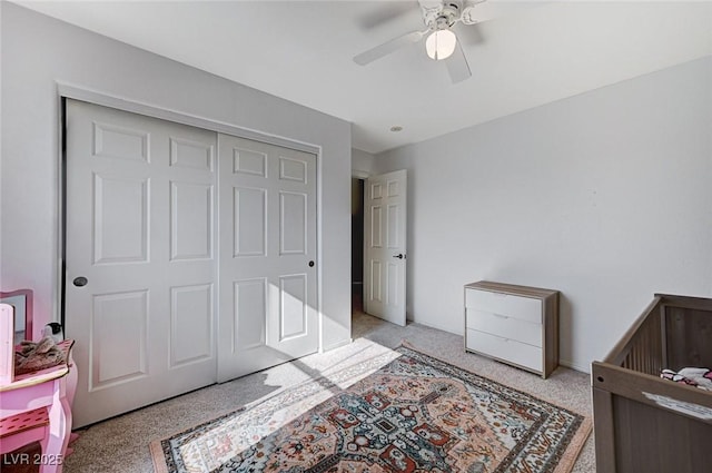 bedroom featuring a crib, light colored carpet, a closet, and ceiling fan