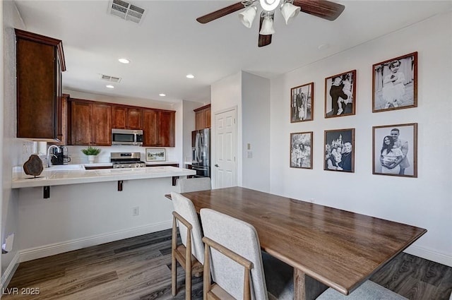 kitchen with appliances with stainless steel finishes, sink, dark hardwood / wood-style flooring, a kitchen breakfast bar, and kitchen peninsula