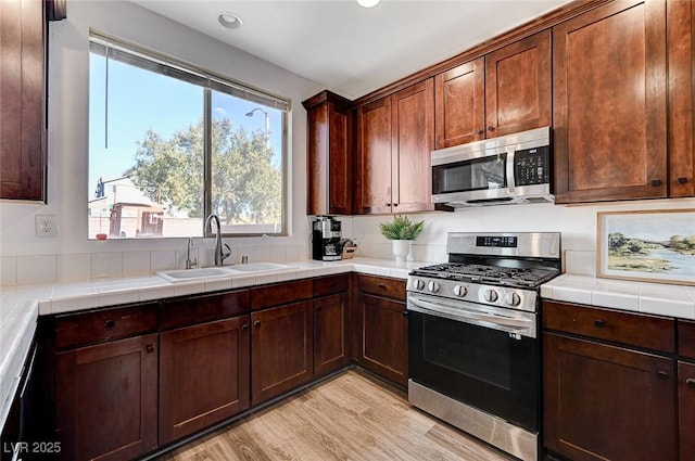 kitchen with sink, tile counters, light hardwood / wood-style floors, and appliances with stainless steel finishes