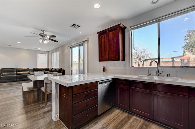 kitchen with dishwasher, sink, tile counters, light hardwood / wood-style floors, and kitchen peninsula