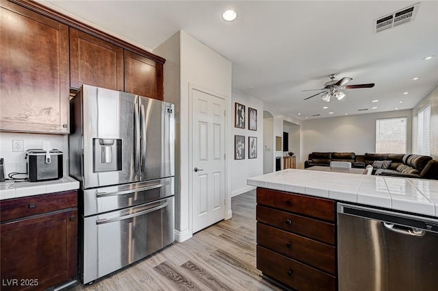 kitchen featuring light hardwood / wood-style flooring, ceiling fan, stainless steel appliances, dark brown cabinetry, and tile countertops