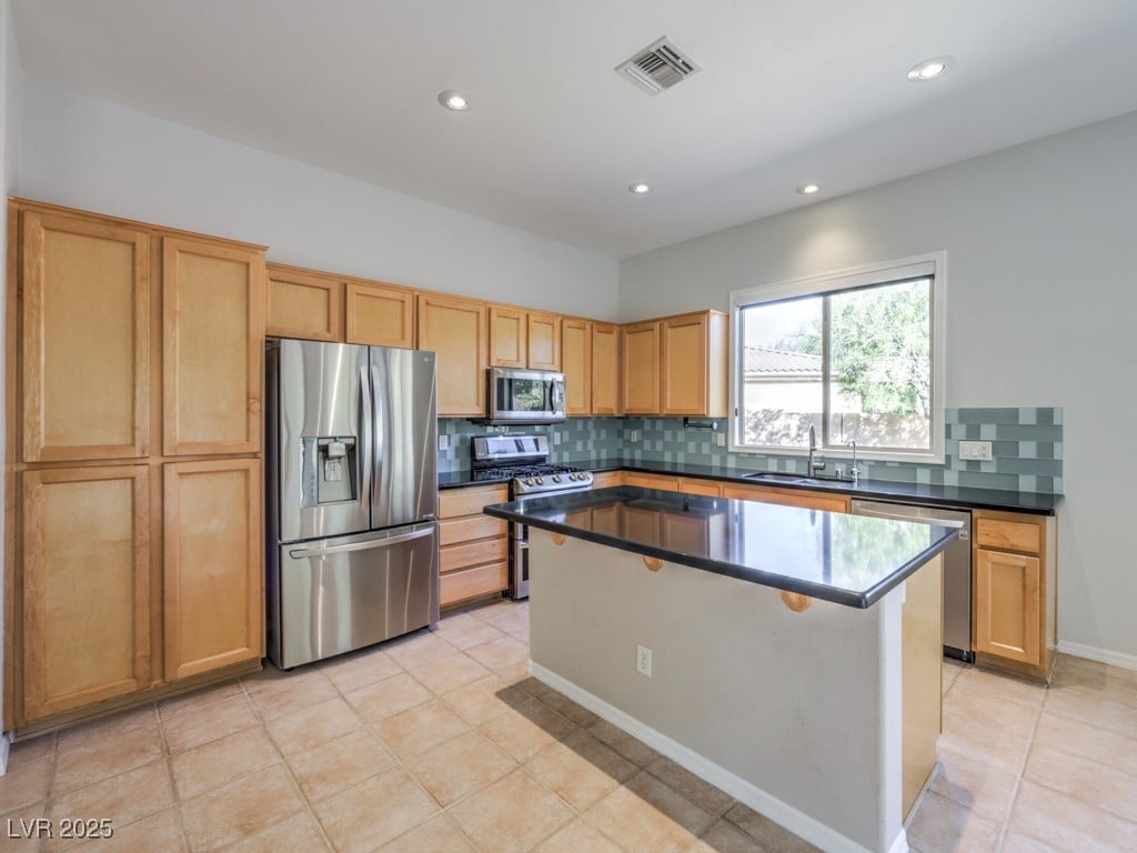 kitchen with light tile patterned flooring, sink, a center island, appliances with stainless steel finishes, and backsplash