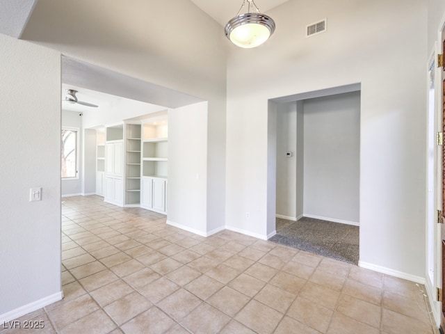 empty room featuring built in shelves, ceiling fan, and light tile patterned flooring