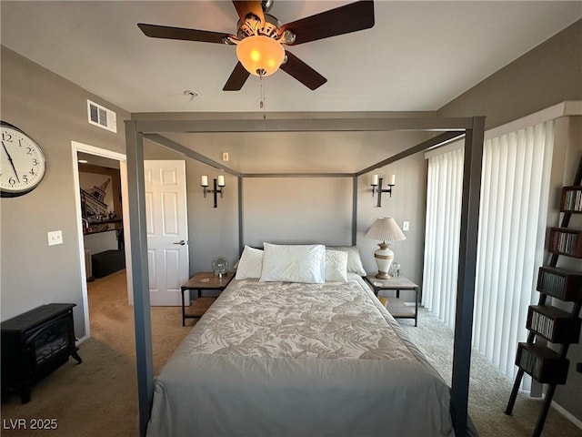 bedroom featuring a wood stove, ceiling fan, and carpet flooring