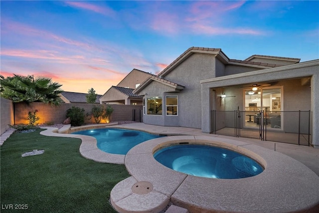 pool at dusk featuring an in ground hot tub and a yard