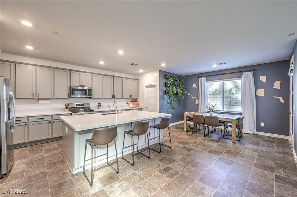 kitchen with sink, a breakfast bar area, appliances with stainless steel finishes, gray cabinetry, and an island with sink