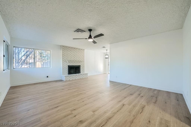 unfurnished living room with a brick fireplace, a textured ceiling, light hardwood / wood-style floors, and ceiling fan