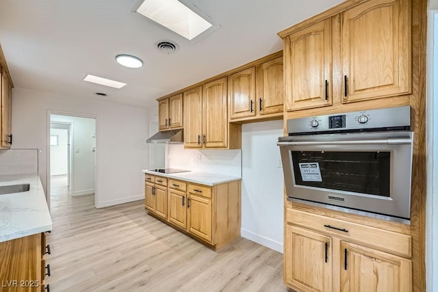 kitchen with a skylight, light hardwood / wood-style floors, light stone countertops, black electric cooktop, and oven