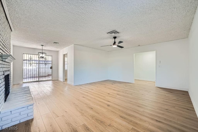 unfurnished living room featuring a brick fireplace, ceiling fan with notable chandelier, light hardwood / wood-style floors, and a textured ceiling