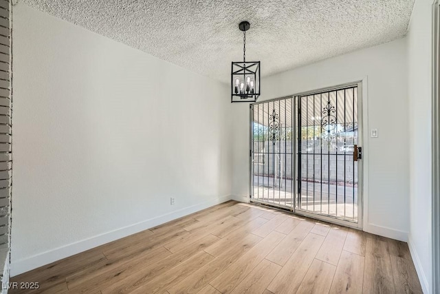 unfurnished dining area featuring an inviting chandelier, a textured ceiling, and light wood-type flooring