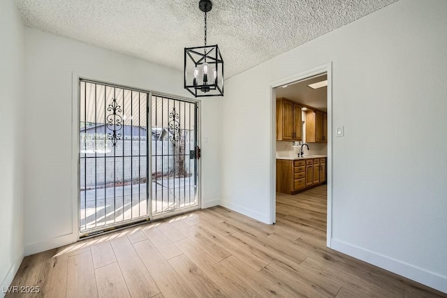 unfurnished dining area with a chandelier, light hardwood / wood-style floors, and a textured ceiling