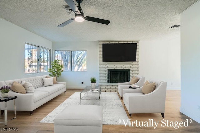 living room with ceiling fan, a textured ceiling, a fireplace, and light hardwood / wood-style floors