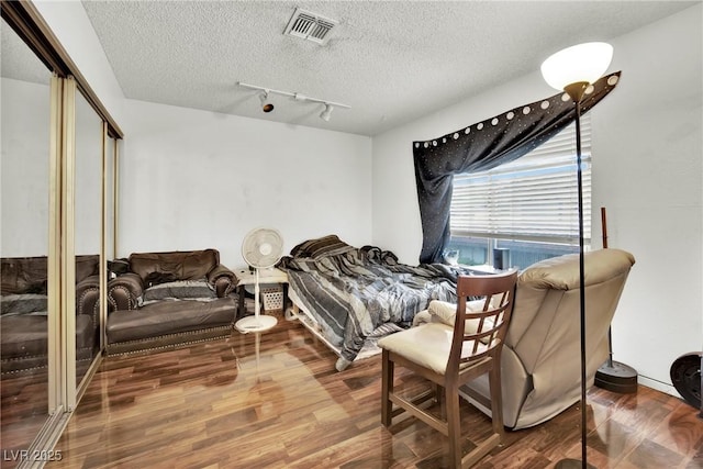 bedroom featuring a closet, rail lighting, hardwood / wood-style floors, and a textured ceiling