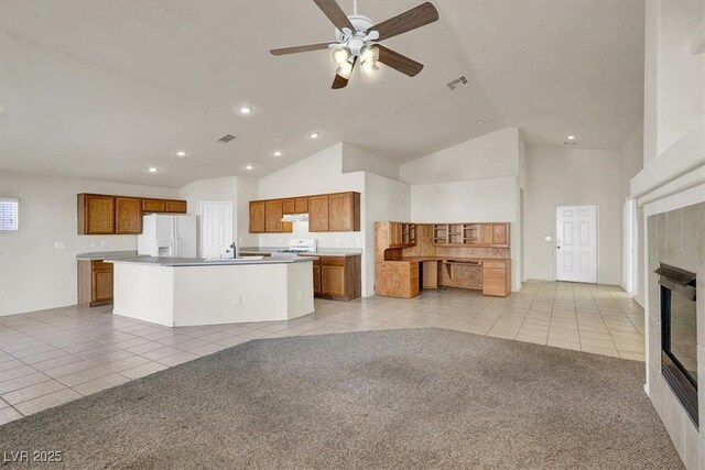 kitchen with light tile patterned floors, a tile fireplace, ceiling fan, white fridge with ice dispenser, and a center island with sink