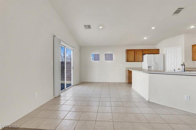 kitchen with lofted ceiling, white fridge with ice dispenser, and light tile patterned floors