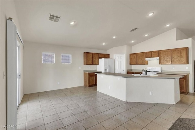 kitchen with lofted ceiling, white fridge with ice dispenser, light tile patterned floors, a kitchen island with sink, and range