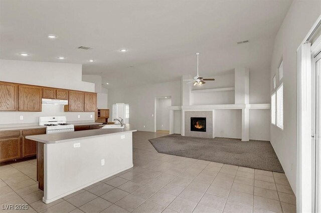 kitchen with sink, light tile patterned floors, white gas range, a tile fireplace, and a kitchen island with sink