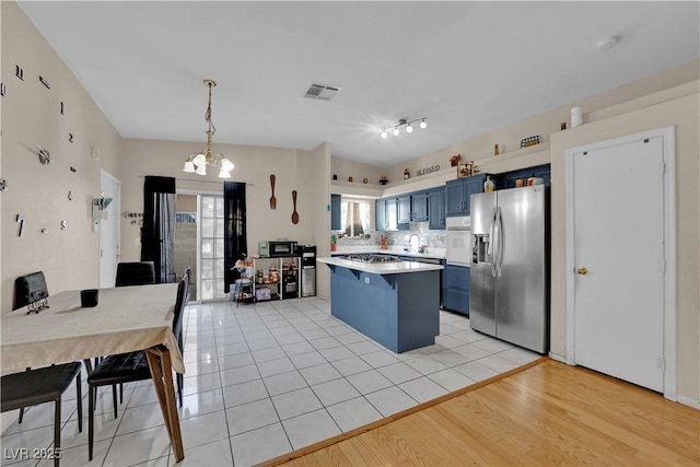 kitchen featuring stainless steel refrigerator with ice dispenser, blue cabinetry, a breakfast bar area, hanging light fixtures, and a healthy amount of sunlight