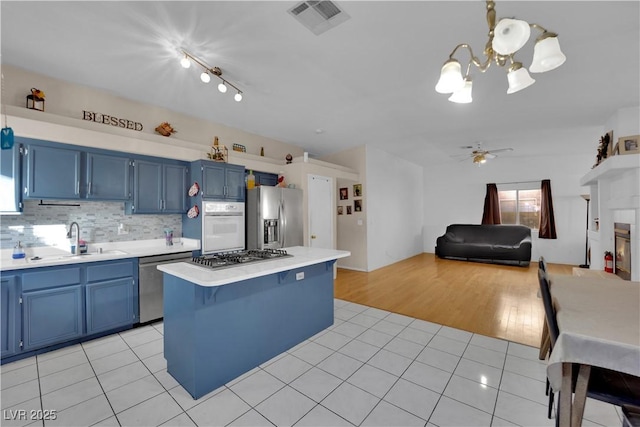 kitchen with light tile patterned flooring, stainless steel appliances, a center island, and blue cabinetry