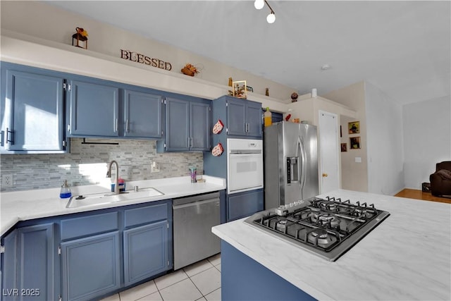 kitchen featuring blue cabinetry, sink, light tile patterned floors, stainless steel appliances, and decorative backsplash