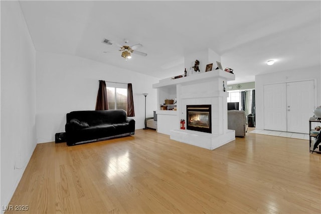 living room featuring a tiled fireplace, ceiling fan, vaulted ceiling, and light wood-type flooring