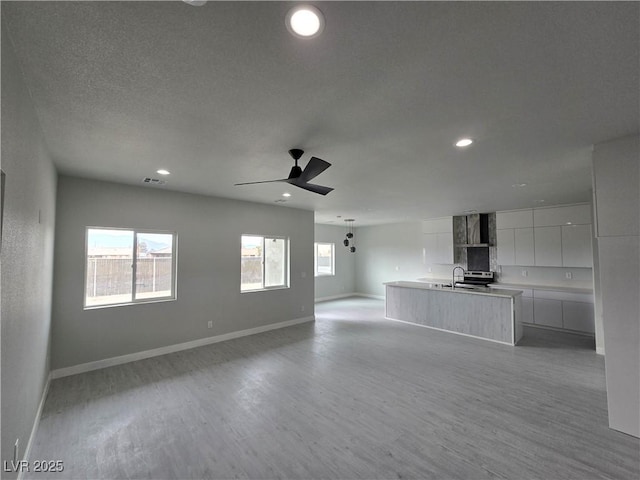 unfurnished living room with ceiling fan, sink, and light hardwood / wood-style floors