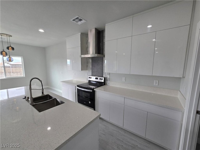 kitchen with electric range oven, pendant lighting, sink, white cabinets, and wall chimney exhaust hood