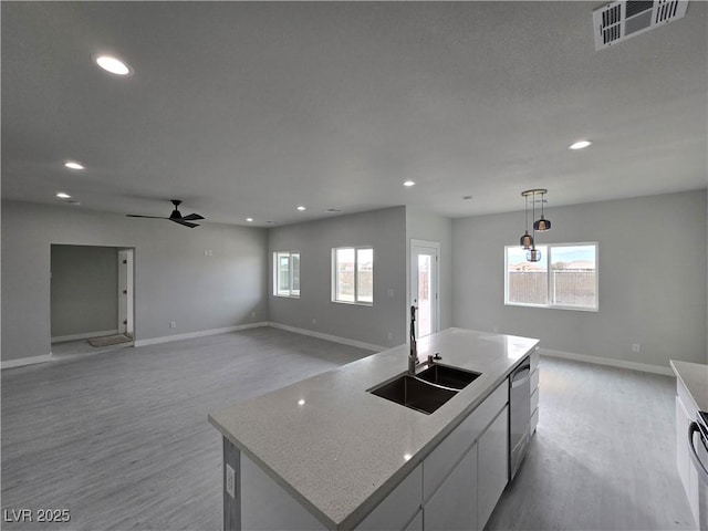 kitchen featuring sink, light hardwood / wood-style flooring, hanging light fixtures, a kitchen island with sink, and white cabinets