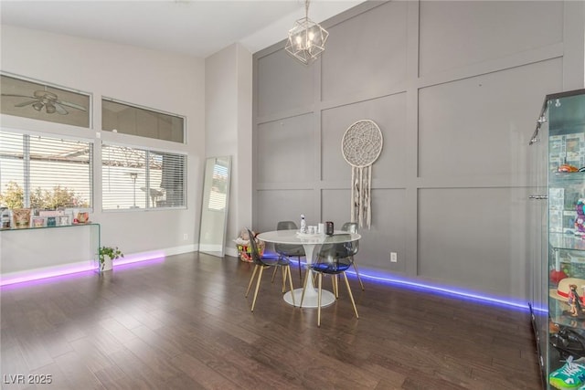 dining area featuring a high ceiling, a decorative wall, wood finished floors, and ceiling fan with notable chandelier