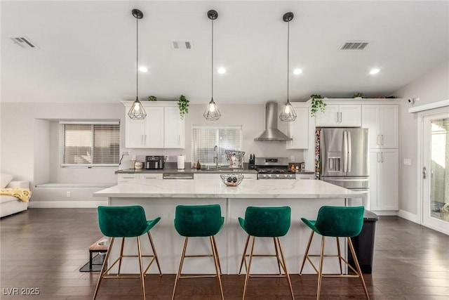 kitchen with a breakfast bar area, stainless steel appliances, visible vents, a center island, and wall chimney exhaust hood