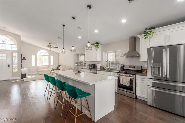 kitchen featuring a breakfast bar area, a kitchen island, open floor plan, appliances with stainless steel finishes, and wall chimney range hood