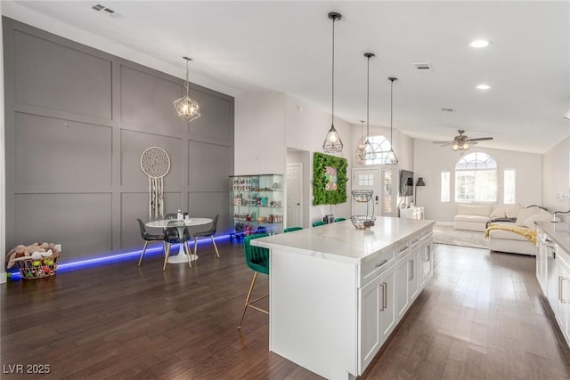 kitchen featuring white cabinets, visible vents, open floor plan, and a decorative wall