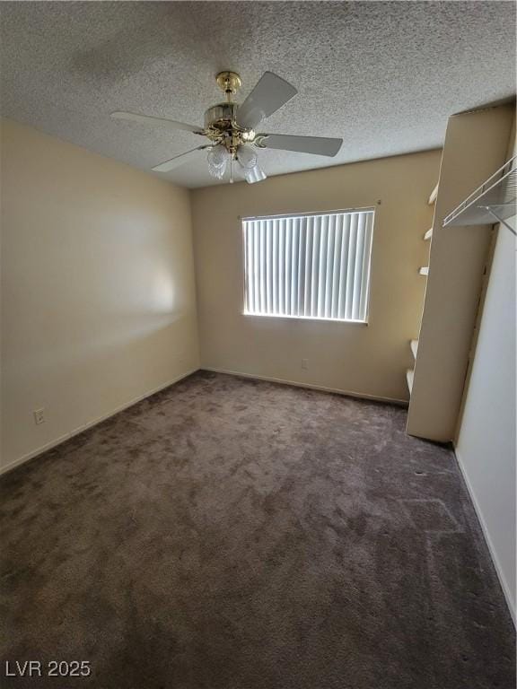 empty room featuring ceiling fan, dark carpet, and a textured ceiling