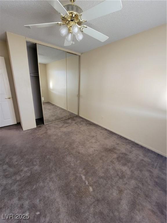 unfurnished bedroom featuring ceiling fan, a textured ceiling, dark carpet, and a closet