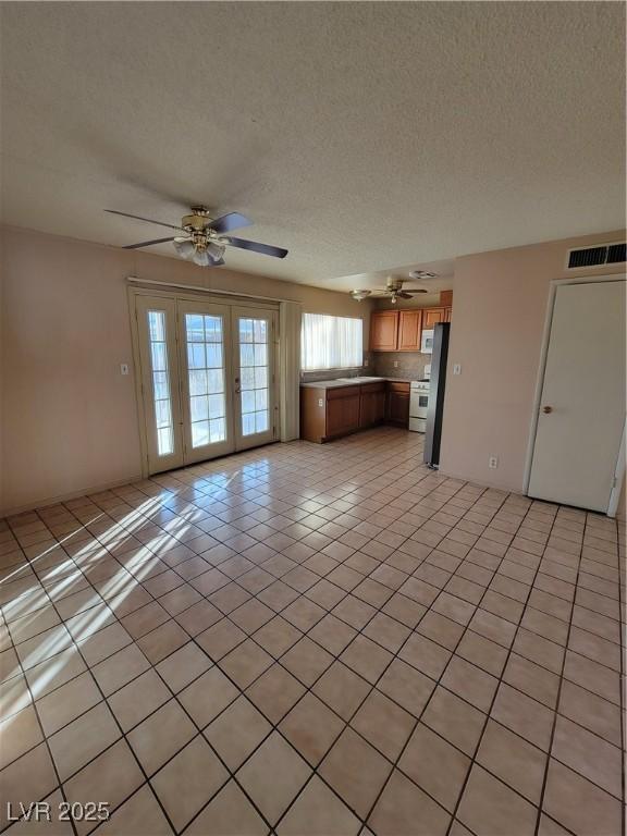 unfurnished living room featuring light tile patterned flooring, ceiling fan, a textured ceiling, and french doors