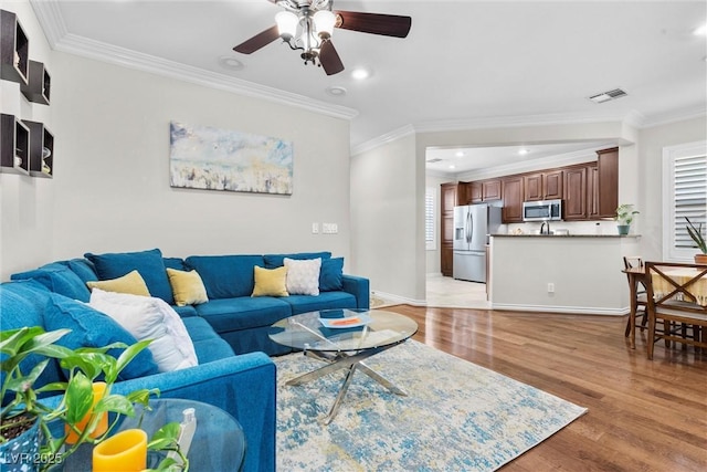 living room featuring crown molding, light hardwood / wood-style flooring, and ceiling fan