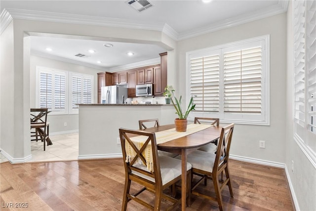 dining area with ornamental molding and light hardwood / wood-style floors