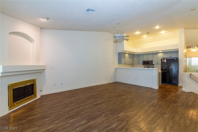 unfurnished living room with lofted ceiling, dark hardwood / wood-style flooring, a tile fireplace, and ceiling fan