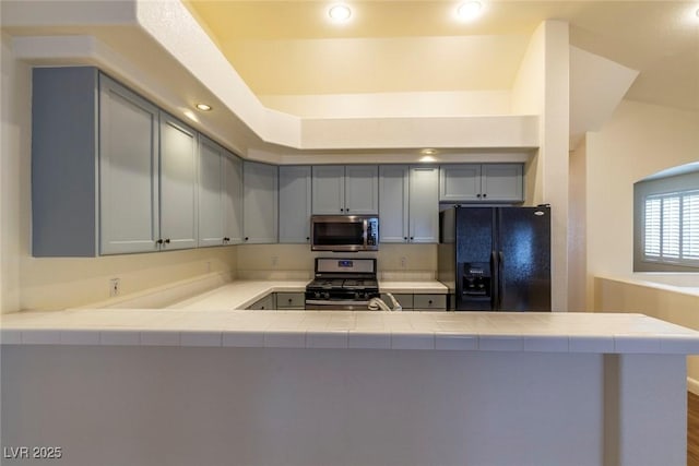 kitchen with stainless steel appliances, kitchen peninsula, hardwood / wood-style floors, and gray cabinetry