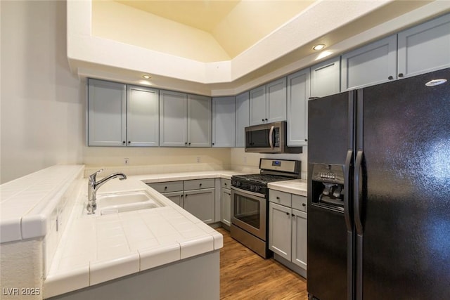 kitchen with sink, stainless steel appliances, tile counters, vaulted ceiling, and kitchen peninsula